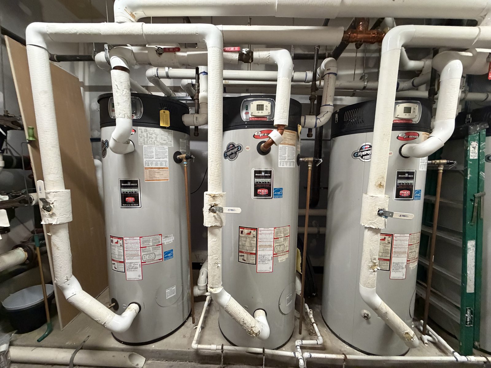 Three Bradford White commercial water heaters side by side in a mechanical room, with insulated piping overhead