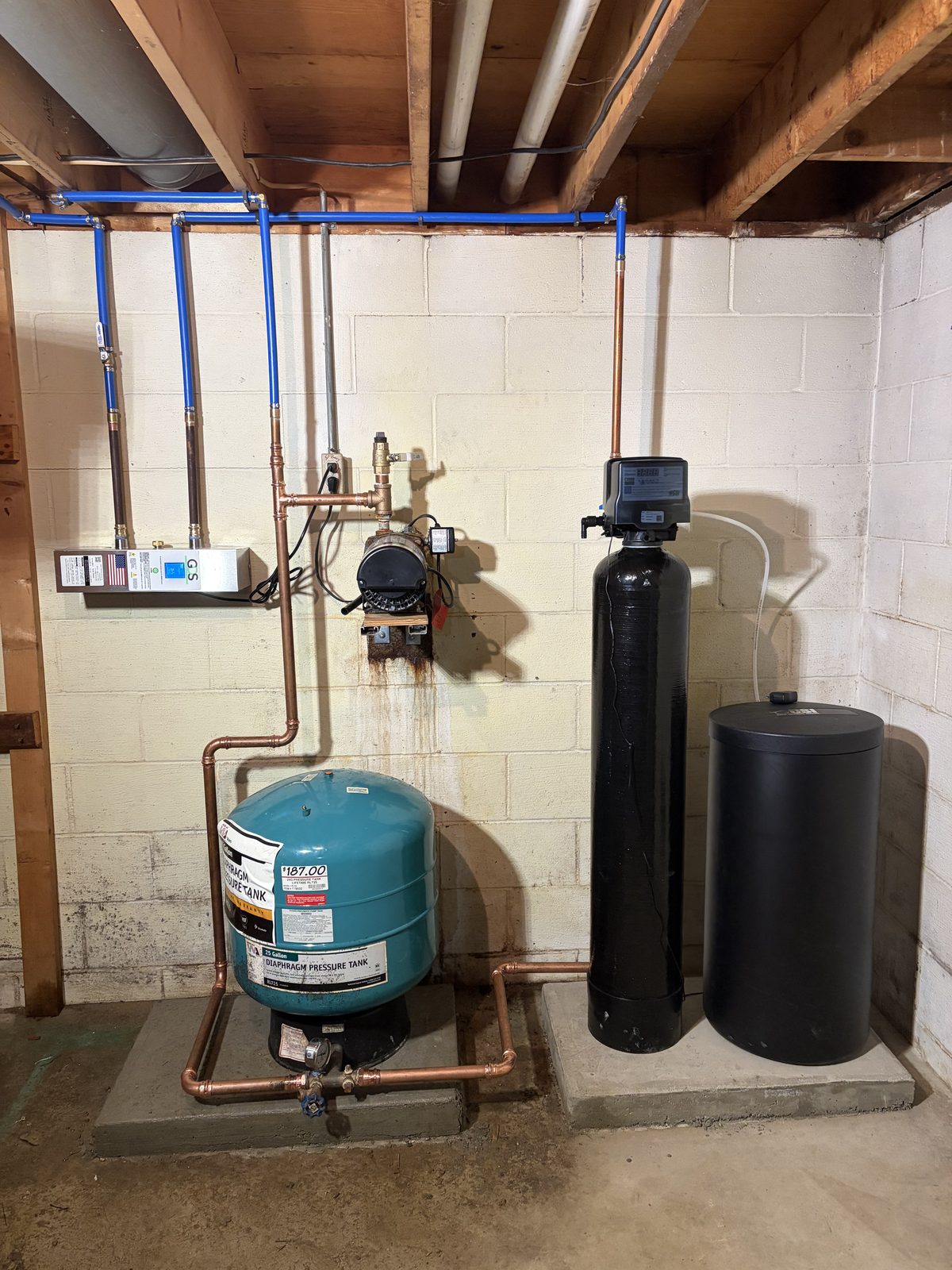 A finished residential well system in a block basement: pressure tank, well pump, water softener and brine tank, plumbed with new copper and blue PEX